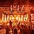 A large crowd at a music festival enjoys a vibrant stage with bright lights and flames, creating an energetic atmosphere.