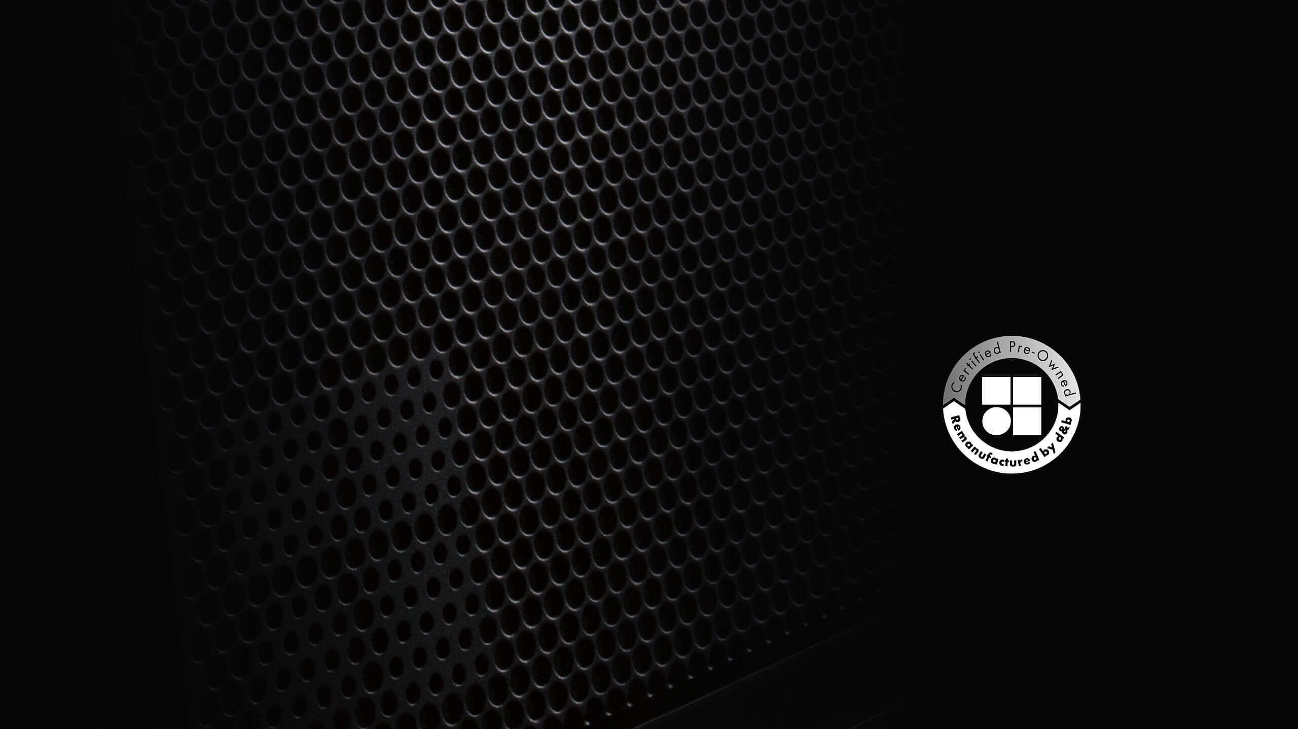 Close-up of a textured black speaker grille with a circular logo in the bottom right corner.