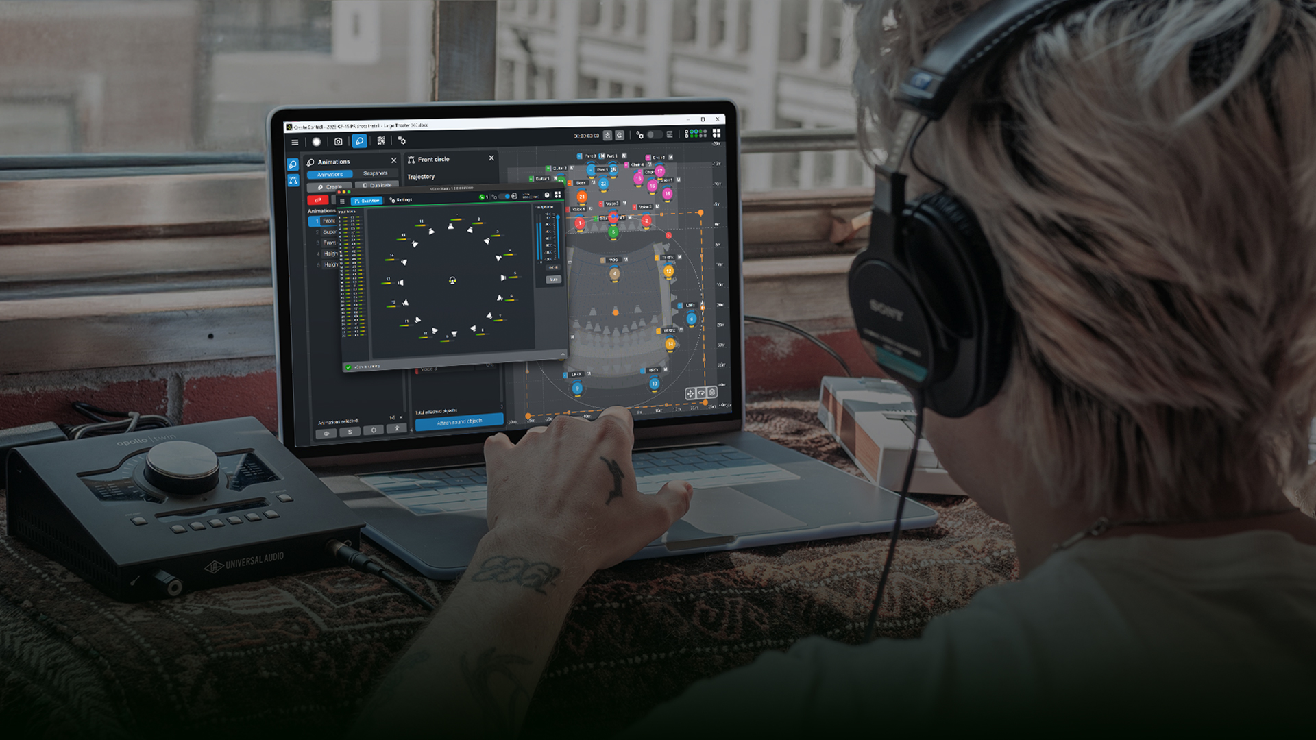 A person wearing headphones interacts with music production software on a laptop, featuring a circular visual display and audio equipment nearby.